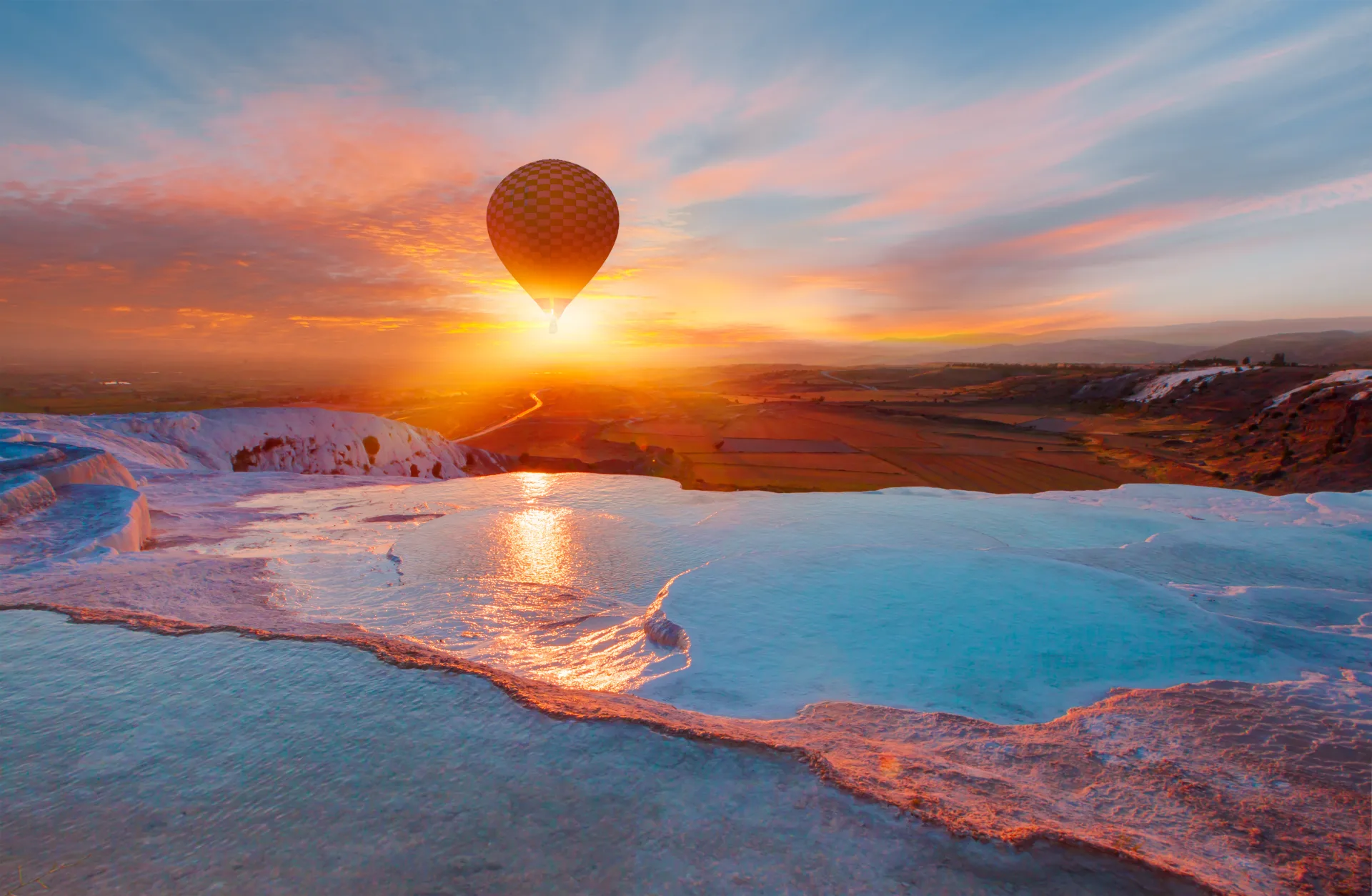 Pamukkale’s travertine pools at sunset with a balloon above